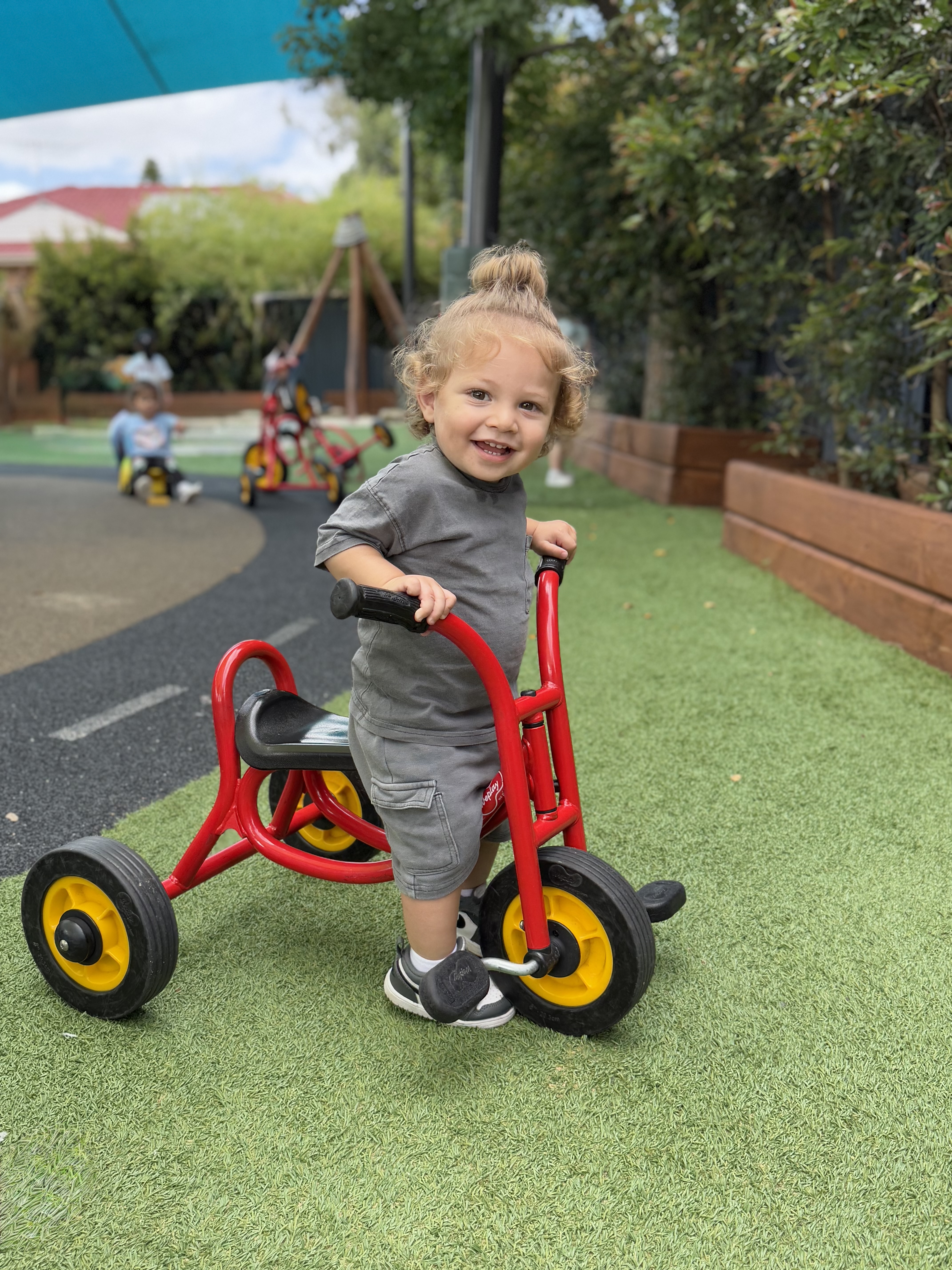 A smiling kid enjoying a ride on a tricycle in the playground.